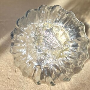 Puede incluir: Un cuenco decorativo de vidrio transparente con un exterior texturizado y acanalado. El centro del cuenco tiene un acabado met&aacute;lico plateado y dorado brillante. El cuenco es redondo y se asienta sobre una superficie de color neutro.