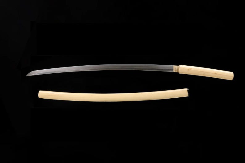 May include: A Japanese katana sword with a curved, silver blade and a light-colored wooden handle. The scabbard is also light-colored wood. The sword is displayed against a black background.
