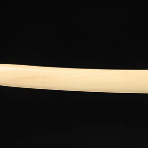 May include: A curved, light-colored wooden object against a black background. The object has a smooth, rounded end and a consistent width along its length. The wood grain is visible.