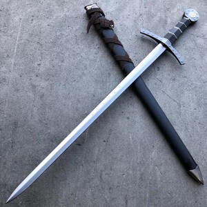 May include: A silver sword with a black leather scabbard and a silver pommel. The sword is crossed over the scabbard.