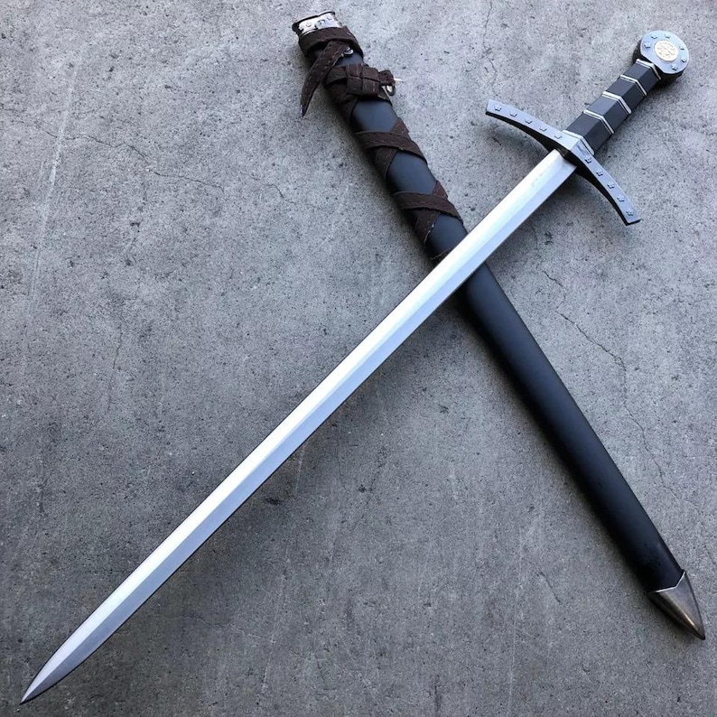 May include: A silver sword with a black leather scabbard and a silver pommel. The sword is crossed over the scabbard.