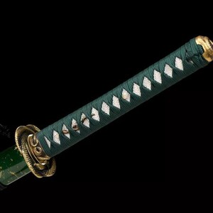 May include: Close-up of a katana handle with a dark green wrap and white diamond-shaped accents. The hilt features gold-colored metal detailing and a black cord. The end cap is gold. The background is black.