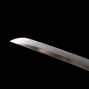 May include: Close-up of a katana blade with a curved edge. The polished steel blade reflects light against a black background. The sword is a traditional Japanese weapon.