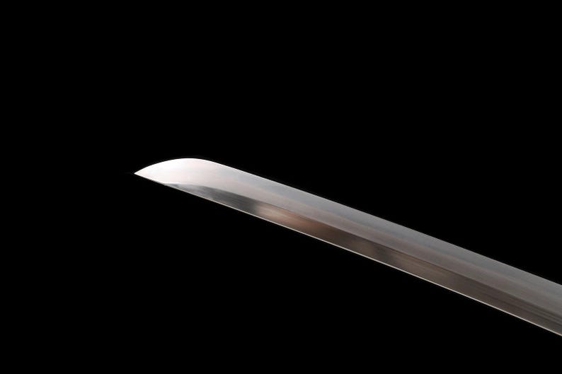 May include: Close-up of a katana blade with a curved edge. The polished steel blade reflects light against a black background. The sword is a traditional Japanese weapon.