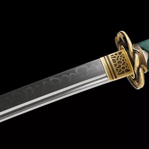 May include: Close-up of a Japanese katana sword. The blade has a wavy pattern and a sharp edge. The hilt is wrapped in green fabric with white diamond-shaped accents. The guard is gold-colored with an intricate design.
