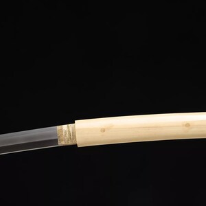 May include: A Japanese katana sword with a light-colored wooden handle and a partially visible blade. The handle is smooth and cylindrical, with a decorative gold-colored band near the blade. The blade is straight and sharp.