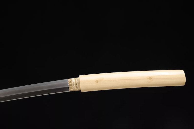 May include: A Japanese katana sword with a light-colored wooden handle and a partially visible blade. The handle is smooth and cylindrical, with a decorative gold-colored band near the blade. The blade is straight and sharp.