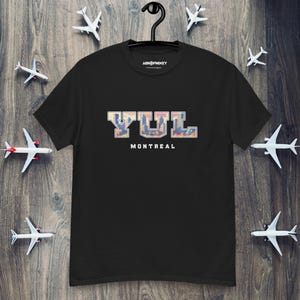 May include: Black t-shirt featuring a graphic of the letters YUL in a college font, with a cityscape inside the letters. The text "MONTREAL" is below the letters.