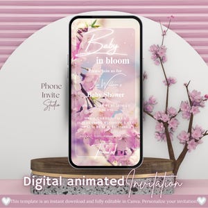 May include: A smartphone displays a baby shower invitation with floral accents and the text "Baby in bloom." The phone rests on a wooden and stone pedestal against a pink backdrop. The words "Digital animated Invitation" are at the bottom.