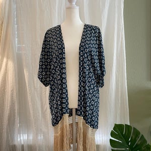 May include: A blue and white floral print kimono with a fringe trim. The kimono has a V-neck and short sleeves.