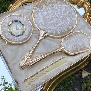 FINER TEMPTRESS - Sminkbordsset i vintage Regency Hollywood-stil. Oanvänd hårborste, spegel, klocka och kam i guldfärgad ask.