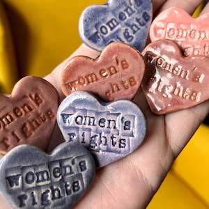 May include: Six heart-shaped ceramic pins with the text "Women's Rights" in a dark blue, light blue, and pink color scheme.