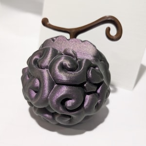 May include: A spherical object with a dark purple, metallic, swirling brain-like texture and a brown, curved stem extending from the top. The surface features deep, rounded ridges and grooves that create a complex, repeating pattern across the sphere.
