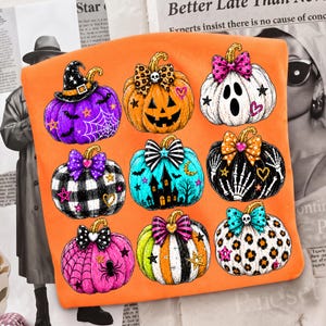 May include: An orange t-shirt featuring a graphic print of nine stylized pumpkins. The pumpkins display various Halloween-themed patterns including a witch hat, a ghost, a haunted house, skeleton hands, spider webs, leopard print, and bows.