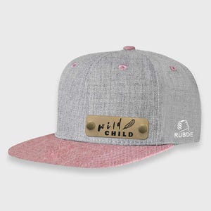 May include: A gray and pink baseball cap with a gold metal plate that says "wild child" with a feather design. The cap is made by the brand Rubde.
