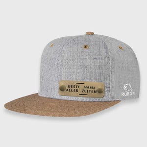 May include: A gray and brown baseball cap with a metal plate that reads "Beste Mama Aller Zeiten". The cap has a cork brim and a small logo on the side.