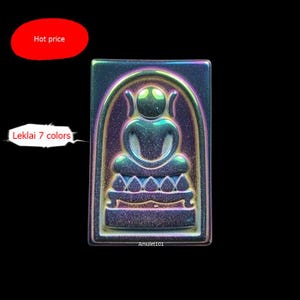 May include: A rectangular, iridescent amulet featuring a seated Buddha figure within an arched frame. The amulet has a textured surface and displays a spectrum of colors, with the text "Leklai 7 colors" visible. The background is black.