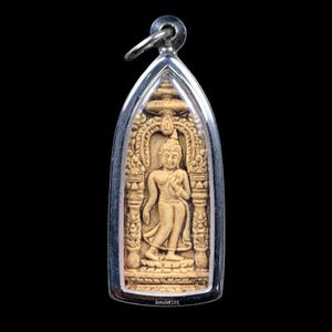 May include: A beige Buddha pendant encased in a silver-colored frame. The pendant features a detailed carving of a standing Buddha figure within an ornate archway. The text "Amulet101" is visible at the bottom.