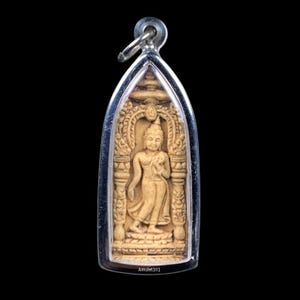 May include: A beige Buddha amulet pendant with a silver-colored frame. The pendant features a detailed carving of a standing Buddha figure within an arched frame. The text "Amulet101" is at the bottom.