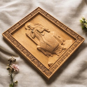 Op de afbeelding: Een rechthoekige houten wandplaat met een reliëfsnijwerk van een bebaarde figuur in versierde gewaden die een boek vasthoudt. De rand vertoont ingewikkelde geometrische patronen en de Griekse tekst luidt Agios Grigorios Palamas.