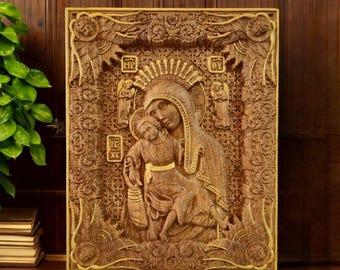 May include: A carved wooden religious icon depicting the Virgin Mary and child. The icon is framed with ornate carvings and features gold accents. The figures are rendered in a detailed, relief style, with intricate patterns and textures throughout the design.