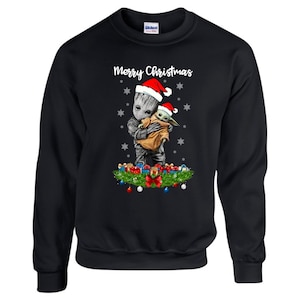 May include: Black Christmas sweatshirt featuring a graphic of a green alien character wearing a Santa hat and holding a smaller green alien character wearing a Santa hat. The text "Merry Christmas" is printed above the graphic.