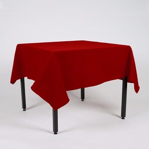 May include: A red tablecloth draped over a square table with black legs. The tablecloth is smooth and has a slight sheen.