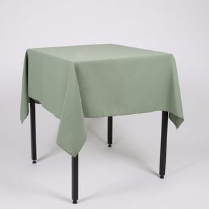 May include: A sage green tablecloth draped over a square table with black metal legs.