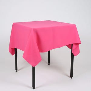 May include: A square pink tablecloth draped over a black table with four legs.