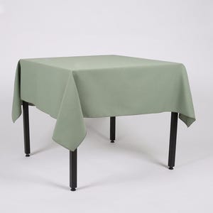 May include: A square green tablecloth draped over a table with black legs. The tablecloth is smooth and has a slight sheen.