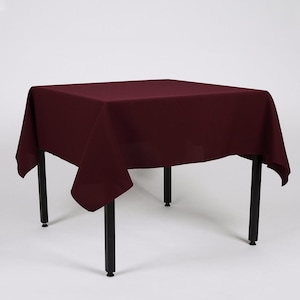May include: A burgundy square tablecloth draped over a black metal table with four legs.