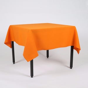 May include: Orange square tablecloth draped over a black metal table with four legs.