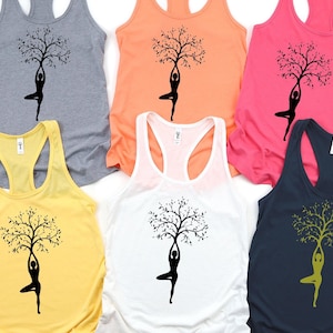 May include: Five tank tops with a yoga pose silhouette holding a tree with branches and leaves. The tank tops are in different colors: gray, peach, pink, yellow, and navy blue.