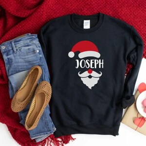 May include: Black sweatshirt with a white Santa Claus graphic and the name "Joseph" in white letters.