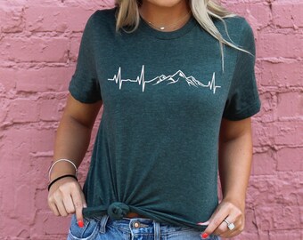 Könnte beinhalten: Ein dunkelgrünes T-Shirt mit einer weißen Bergkette und einem Herzschlag-Motiv. Die Grafik lautet "Mountain Heartbeat".