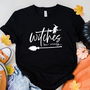 May include: Black t-shirt with white text that reads "Witches be crazy" and a witch flying on a broomstick graphic.