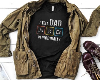 Könnte beinhalten: Schwarzes T-Shirt mit einer weißen Grafik, auf der "I tell Dad Jokes Periodically" steht. Die Grafik zeigt die chemischen Symbole für "Jo", "K" und "Es" in bunten Kästchen.