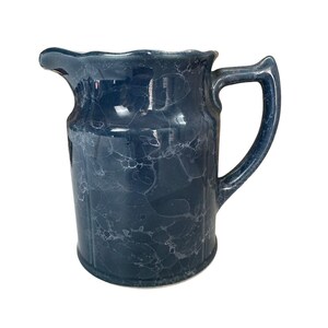 May include: A blue ceramic pitcher with a marbled glaze. The pitcher has a wide mouth and a handle.