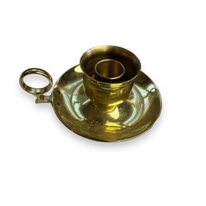 May include: A gold metal candle holder with a round base and a ring handle. The holder has a small inner ring to hold a candle.