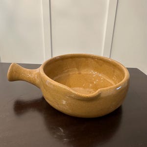May include: A brown ceramic serving dish with a single handle. The dish is glazed and has a speckled texture.