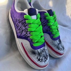 Puede incluir: Zapatillas personalizadas con temática del Joker. Las zapatillas tienen una base blanca con detalles morados y verdes, cordones verdes y la frase "Why So Serious?" en la puntera. El diseño incluye el texto "Ha Ha Ha".
