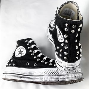 Può includere: Sneakers Converse nere alte con borchie argentate e suola platform bianca. Le scarpe hanno un aspetto vissuto e il logo Converse All Star è visibile sul lato.