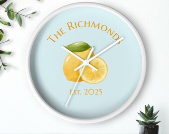 May include: A round wall clock with a white frame. The clock face is light blue with a watercolor illustration of a lemon and a half lemon. The text "THE RICHMONDS" and "EST. 2025" are in gold.