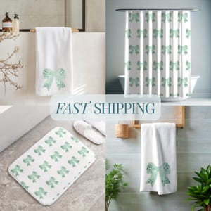 May include: A set of bathroom accessories featuring a green and white bow pattern. The set includes a shower curtain, bath mat, hand towel, and bath towel.