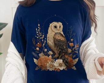 Könnte beinhalten: Marineblaues Langarmshirt mit Eulen-Illustration und dem Wort "NAVY". Die Eule hat braune und weiße Federn, umgeben von orangefarbenen und cremefarbenen Blumen. Ein bequemes Shirt für den Alltag.