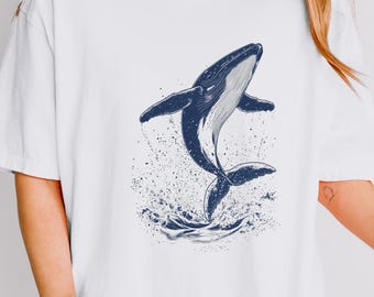 May include: White oversized t-shirt featuring a blue whale jumping out of the water graphic.