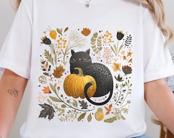 Könnte beinhalten: Weißes T-Shirt mit einem schwarzen Katzen- und Kürbis-Motiv. Die Katze sitzt neben einem gelben Kürbis, umgeben von Herbstblättern und -blumen. Das Wort "WHITE" ist oben rechts aufgedruckt.