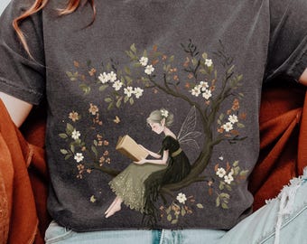 Camiseta de manga larga con diseño de hada leyendo un libro en un árbol, estilo cottagecore. Camiseta gráfica con colores naturales y reconfortantes para amantes de los libros. Top estilo fairycore.
