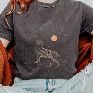 May include: Dark gray t-shirt with a gold tiger illustration, a yellow moon, and stars. The word "PEPPER" is printed at the top right. The shirt is short-sleeved and has a vintage, worn look.
