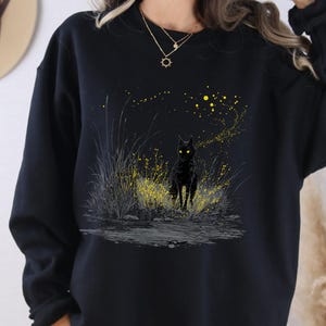 May include: Black sweatshirt with a graphic of a black cat with glowing yellow eyes in a field of yellow and grey grass. The word "BLACK" is printed at the bottom of the sweatshirt.
